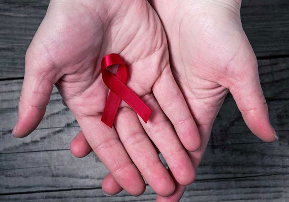 Two hands held together with the palm facing up are holding a red HIV ribbon.
